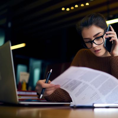 Young woman studying and talking on the phone with papers and laptop.