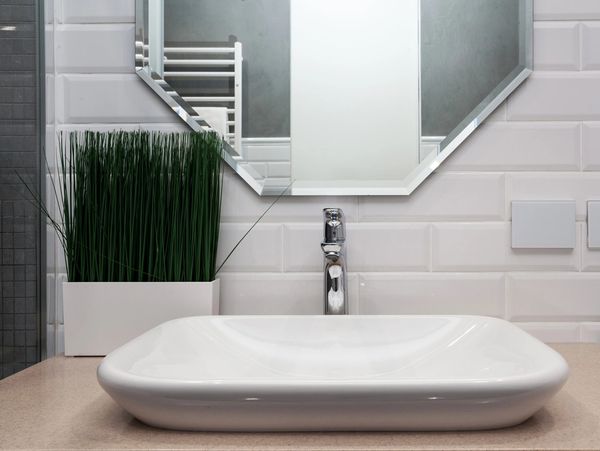 Clean bathroom sink with modern mirror and plant.