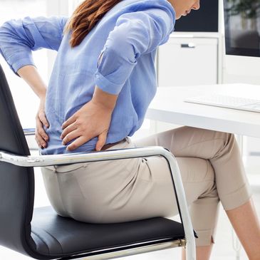 A woman at a desk holding her sore back.