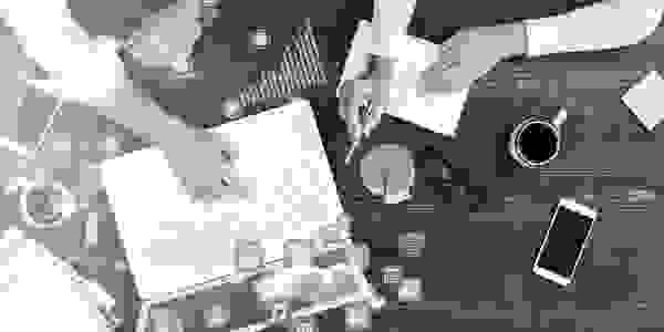 Image of 2 pairs of hands working over a computer keyboard. Represents building a marketing plan. 