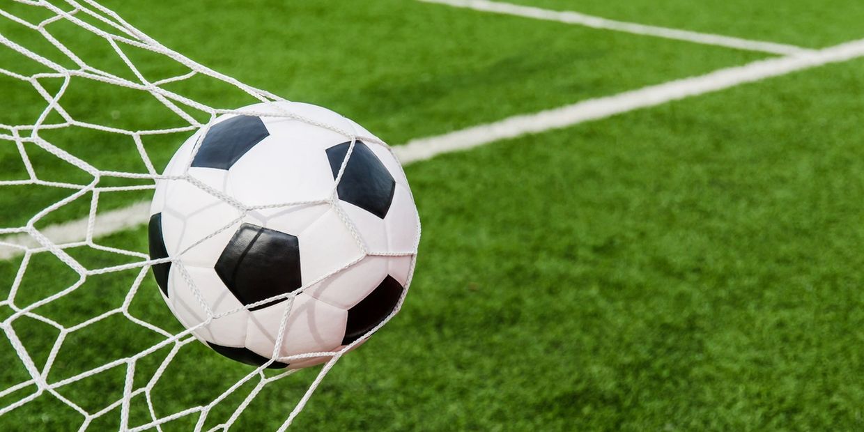 A soccer ball caught in the net on a green field.