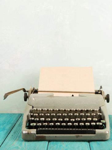 Vintage typewriter with blank paper on turquoise wooden table.