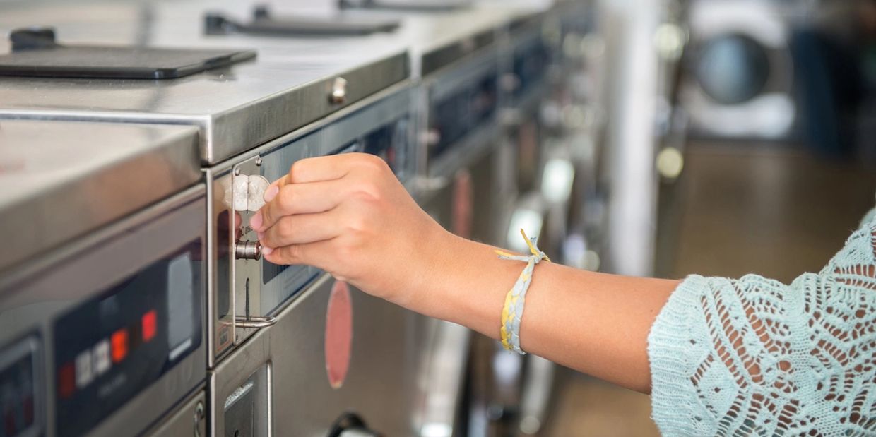 person putting a quarter into a washer machine. Easy Breezy Laundromat. Laundromat near me, 