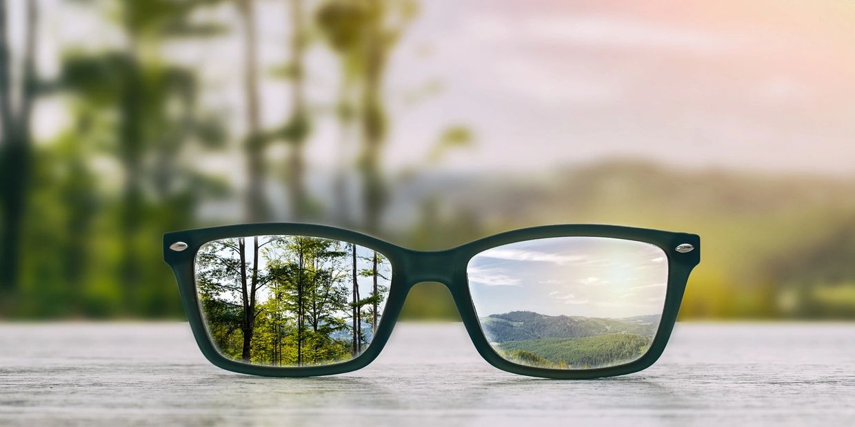 Glasses focusing on a clear outdoor landscape with trees and hills.