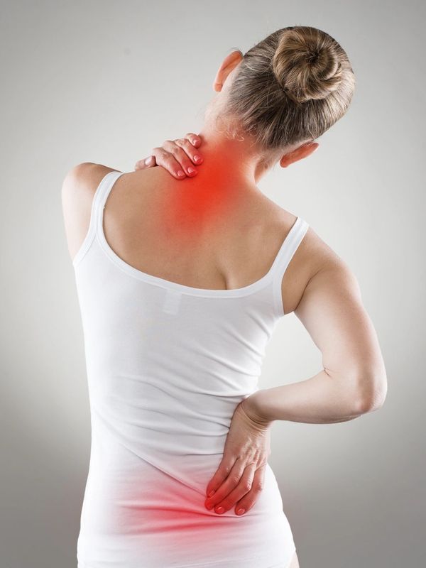 Woman in white tank top holding neck and lower back in pain, highlighted red areas.