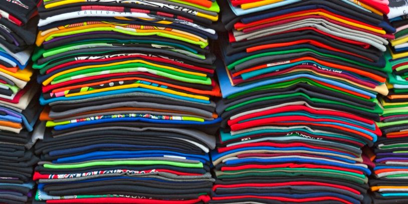 Neatly stacked piles of colorful folded t-shirts.