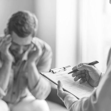 An upset man with his hands on his head and a therapist taking notes