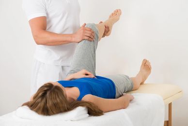 Therapist assisting woman with leg stretch on treatment table.