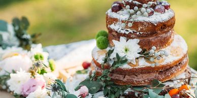 A rustic naked cake decorated with flowers and berries on a table.