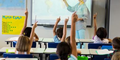Students eagerly raise their hands in a classroom during a lesson.