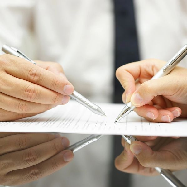 Two hands holding pens over a document, preparing to sign.