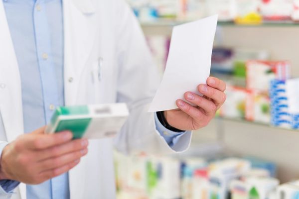 Pharmacist checking prescription with medication box in a pharmacy.