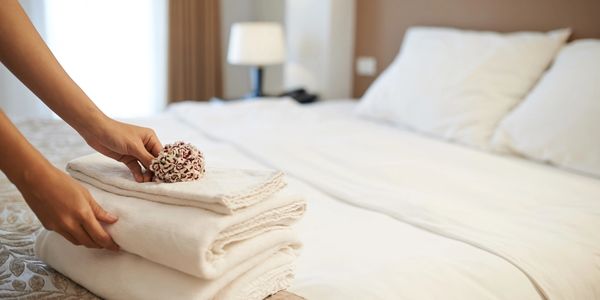 woman folding fresh linens, delicately placing materials on top of made bed