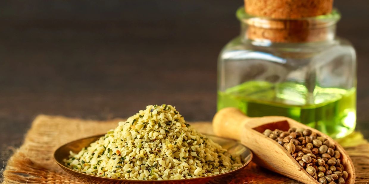 A plate of grains, a scoop of nuts, and a closed jar of a green liquid sitting on a table.