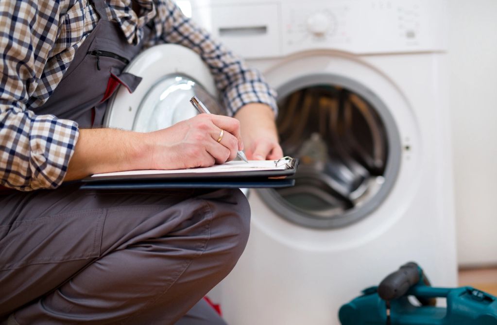 Technician inspecting washing machine and taking notes.