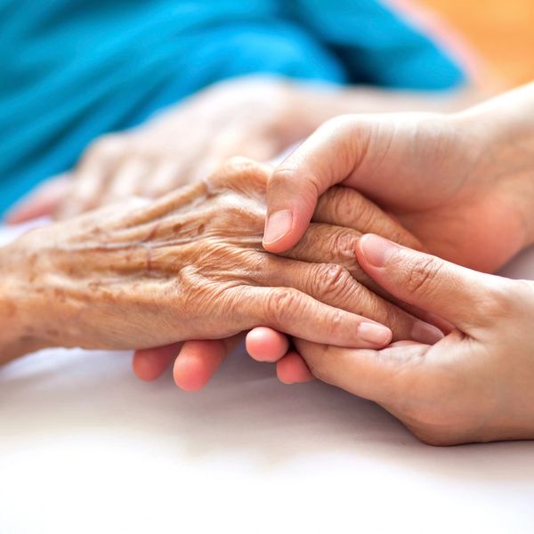 A younger person holding an older person's hand in theirs with compassion.