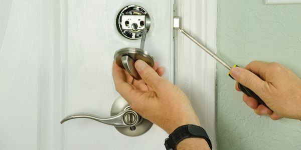 Person fixing a door lock with a screwdriver.