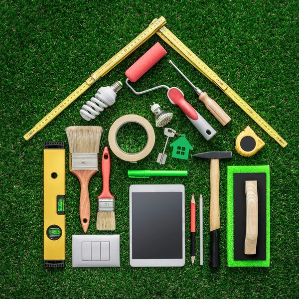 House-shaped arrangement of home improvement tools on green grass.