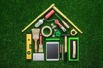 House-shaped arrangement of home improvement tools and gadgets on grass.