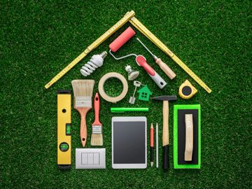 House-shaped layout of various painting and DIY tools on grass.