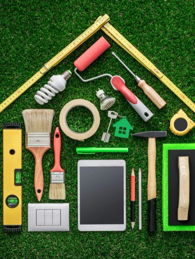 House-shaped arrangement of home improvement tools and gadgets on grass.