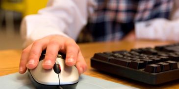 Hand using a computer mouse next to a keyboard.