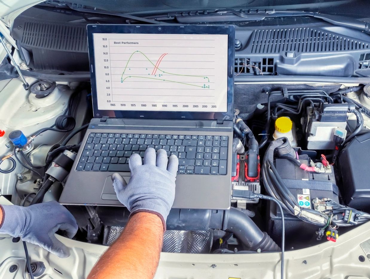 Mechanic diagnosing car engine with laptop showing performance graph.