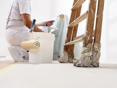 Painter preparing to paint a wall with a roller near a paint bucket and ladder.