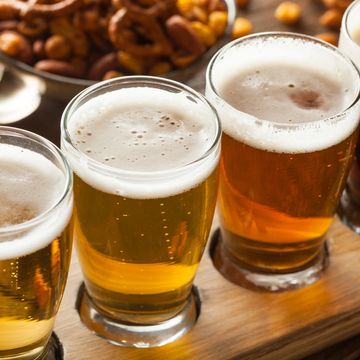 Three glasses of beer with foam on top on a wooden tray.