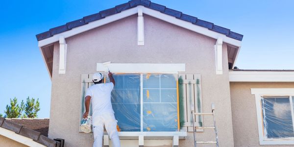 Painter painting the exterior of a house under a clear blue sky.