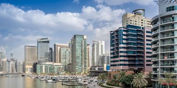Modern waterfront cityscape with yachts and high-rise buildings under a blue sky.