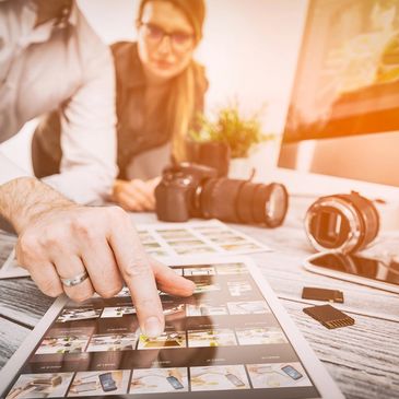 Photo of editorial team around a table where cameras and lenses rest along with photography prints.