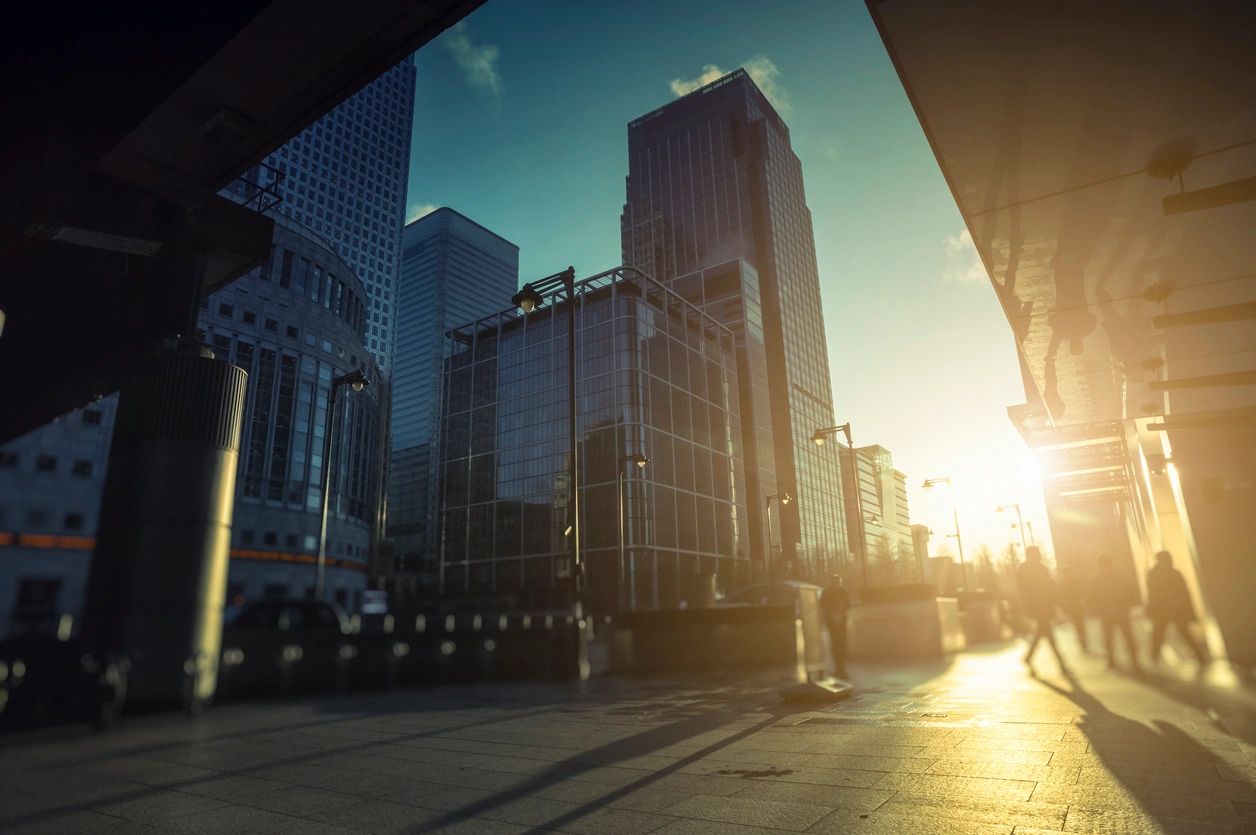 buildings of street in London and the sun shining in between the gaps, people walking 