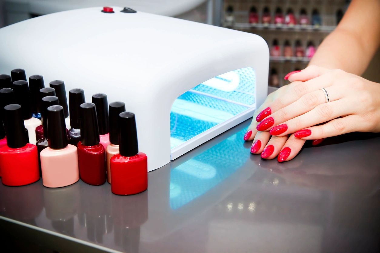 A lady with red nail varnish, a UV nail drier and a selection of nail varnishes