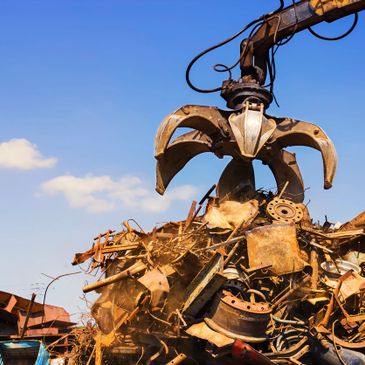 Industrial claw lifting scrap metal at a scrapyard.