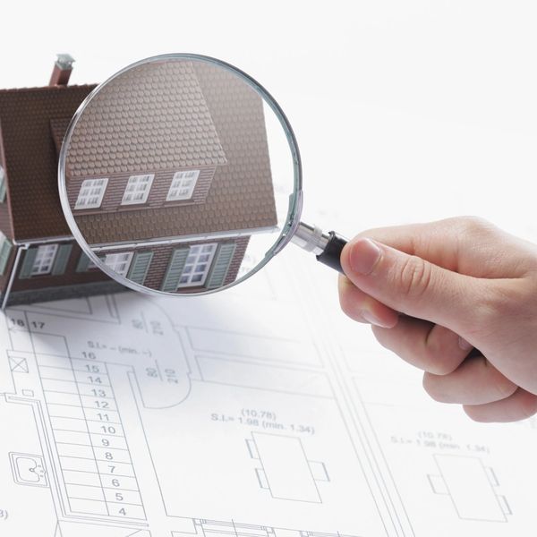 A person holding a magnifying glass over a house.