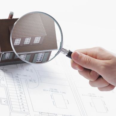 Hand holding magnifying glass over house model and blueprint.