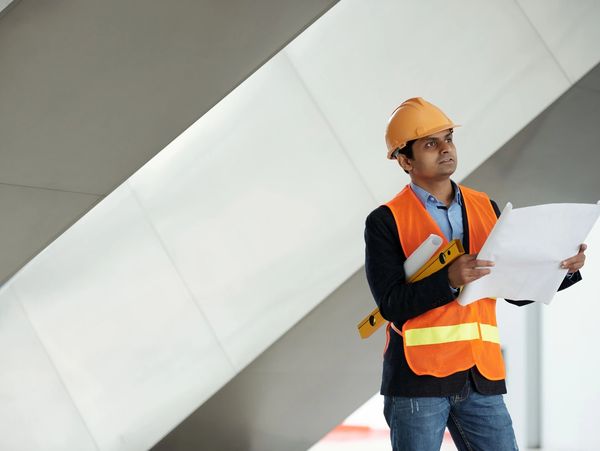 Engineer in safety gear reviewing construction plans indoors.