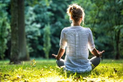 Woman meditating alone in a sunlit forest clearing.