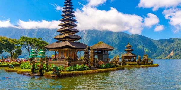 Scenic temple complex on a lake with mountains in the background.