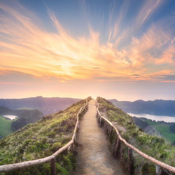Pathway leading through green hills under a radiant sunset sky.