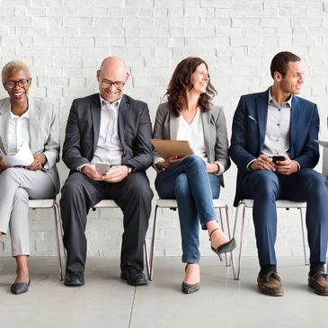 Four professionals sitting and waiting, using digital devices and smiling.