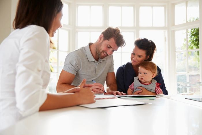 A couple with a baby signing documents with a woman in a bright room.