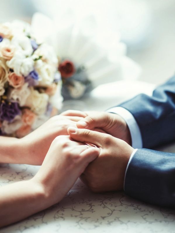 Couple holding hands tenderly with a wedding bouquet in the background.