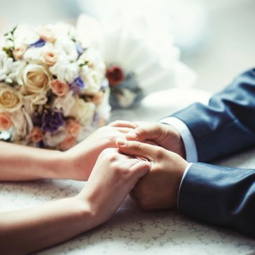 Couple holding hands with wedding bouquet in background.