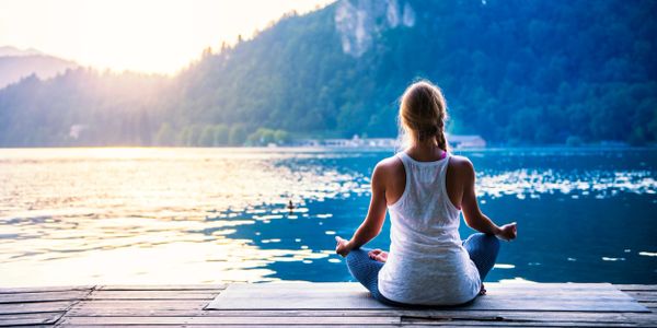 Woman sitting in peaceful meditation on a dock near water, feeling at peace.