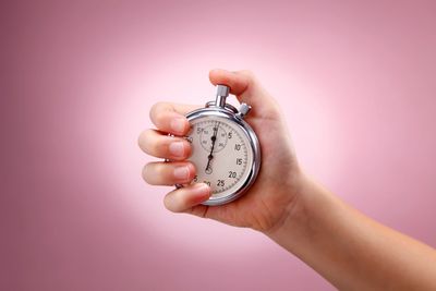 Hand holding a stopwatch against a pink background.