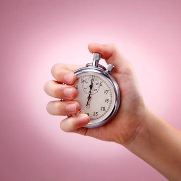 Hand holding a stopwatch against a pink background.