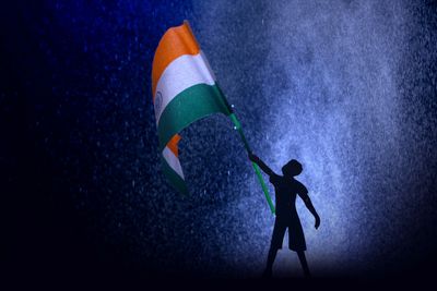 Silhouette of a child waving the Indian flag against a blue misty background.