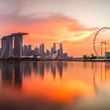 Sunset over Singapore skyline with Marina Bay Sands and the Singapore Flyer reflected in water.